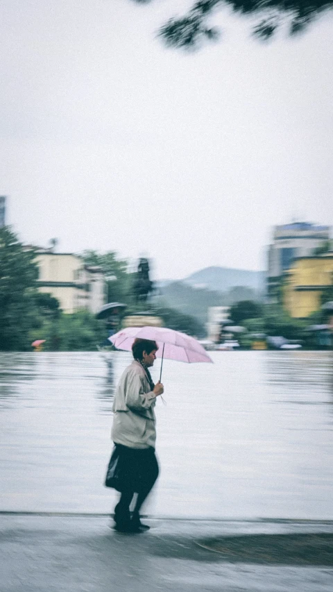 a man walking down a street in the rain with a pink umbrella