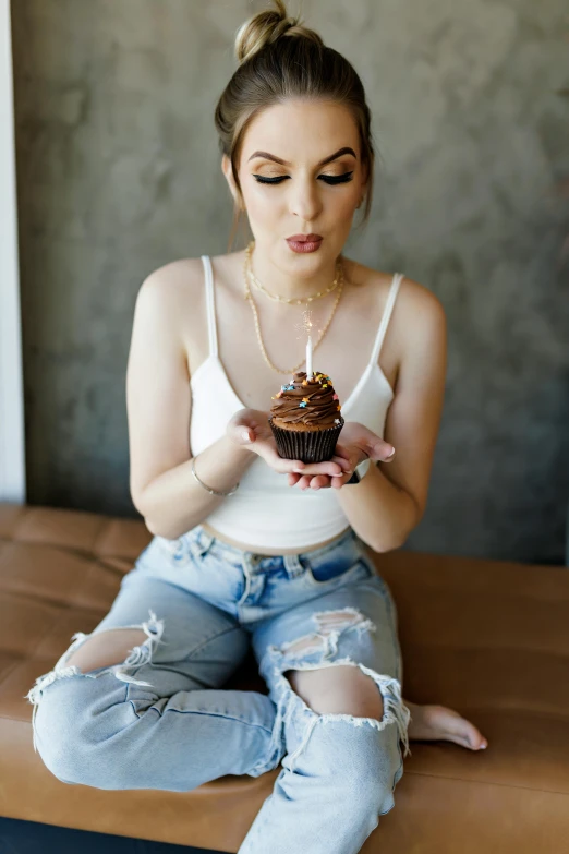 a woman wearing ripped jeans holding a piece of chocolate cupcake