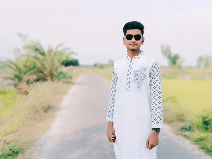 a young man standing on a dirt road near the grass