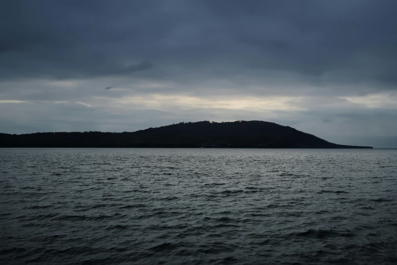 a large body of water with a very small hill in the background