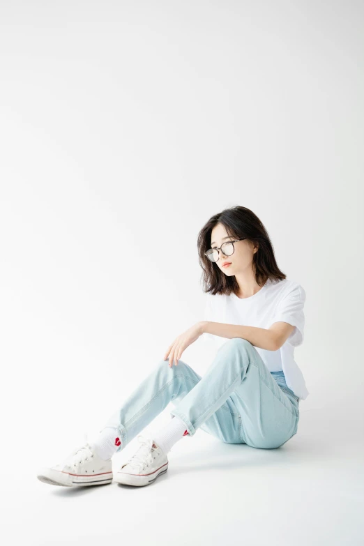 an asian female wearing glasses and blue jeans sits on the floor