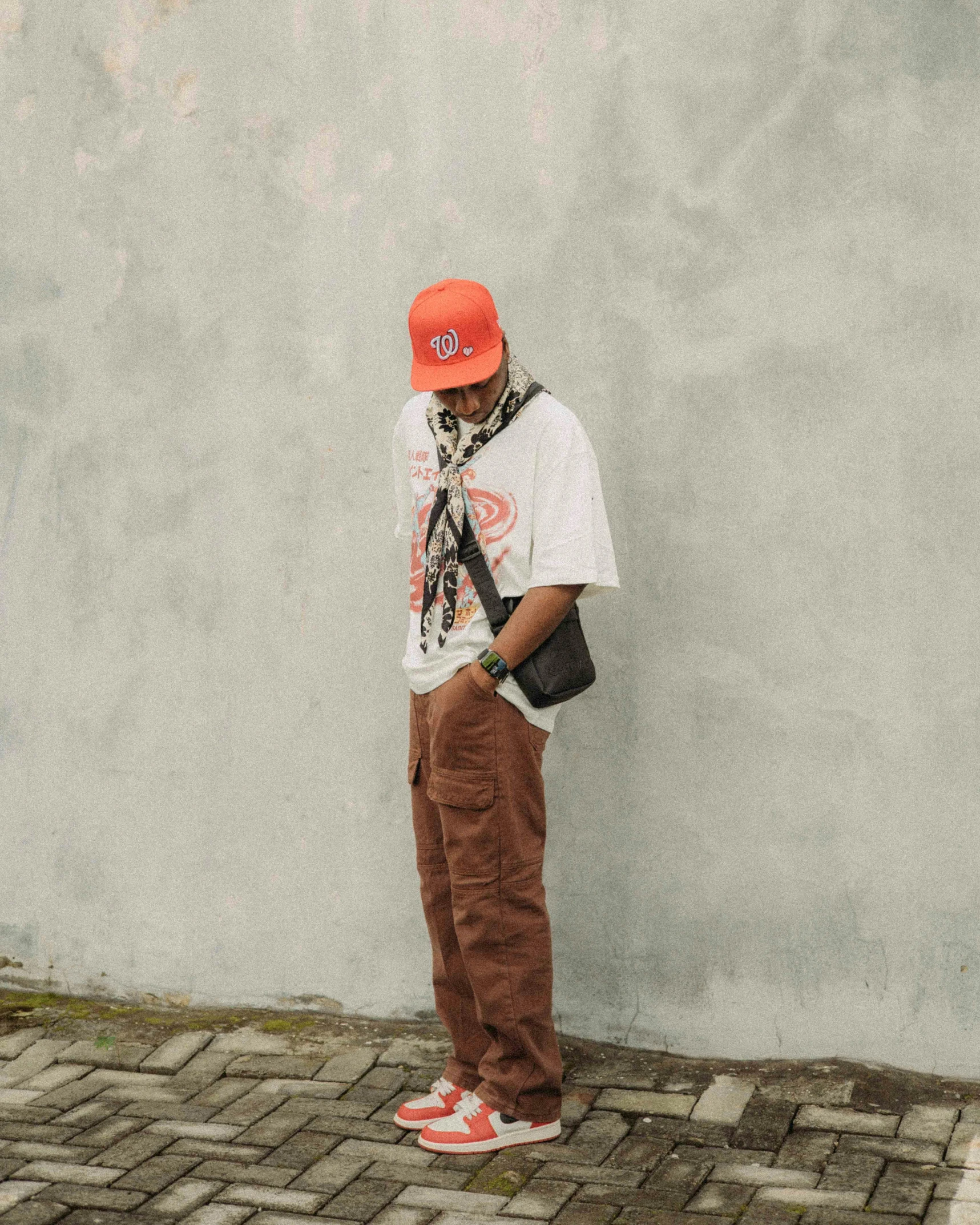 a man stands by the side of a wall while wearing a hat