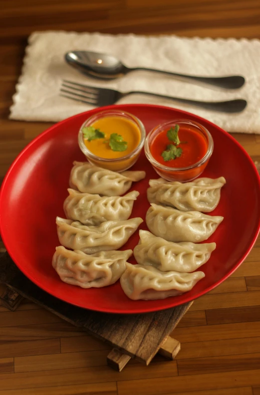 a plate on a table holding dumplings, dipping sauce and two forks