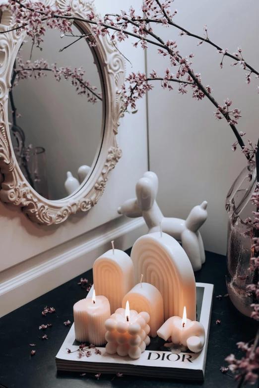 candles placed near a mirror, beside a bouquet of plum blossoms