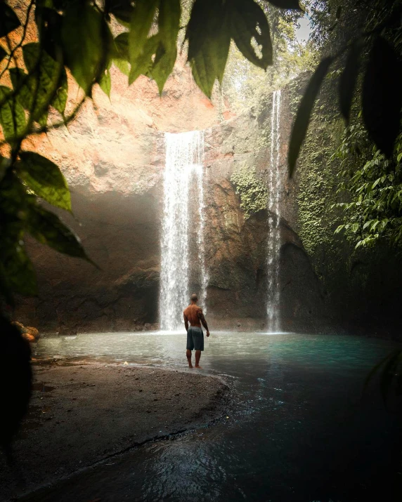 there is a man standing in the water at the base of a waterfall