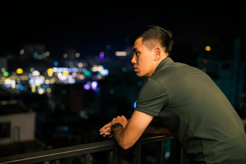 a man leaning against a railing in front of a city skyline at night