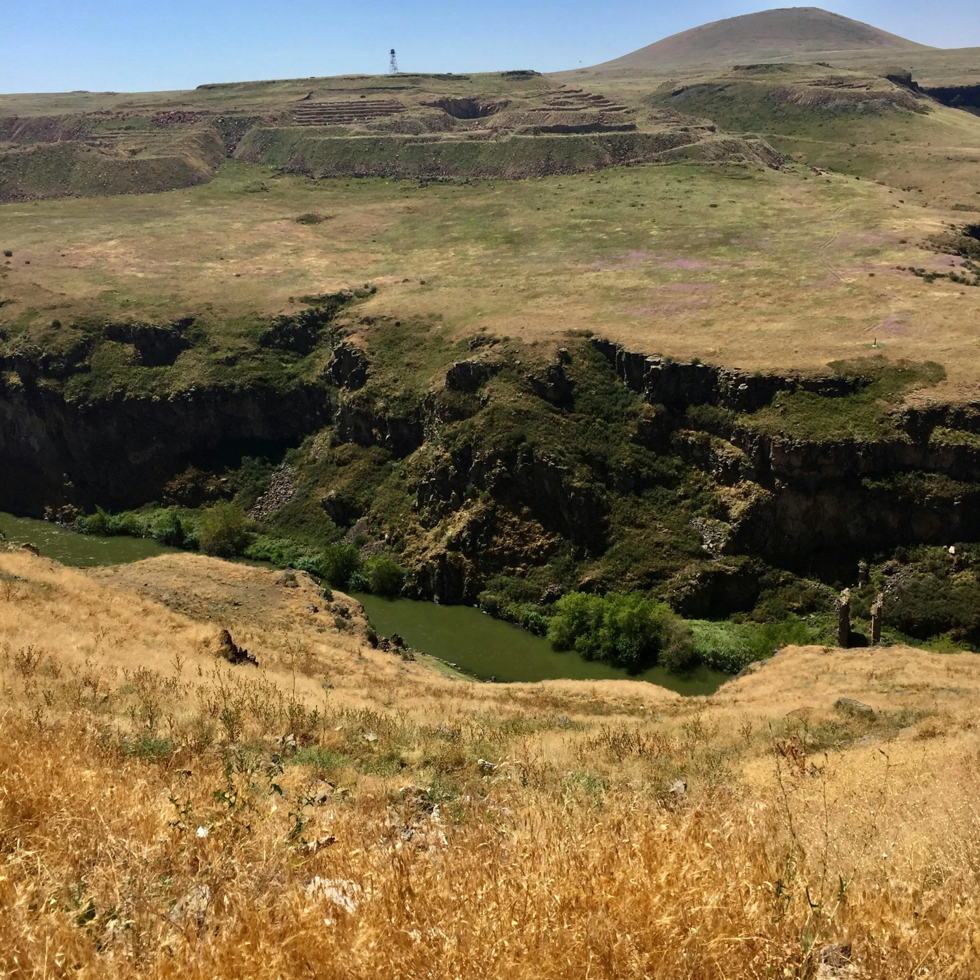 a mountain is shown with lots of grass and a river in the middle of it