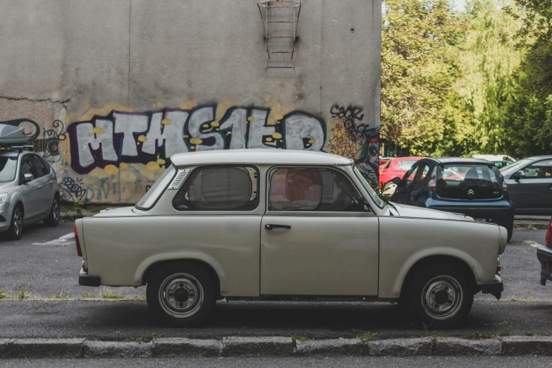 an old white car parked in front of a building with graffiti