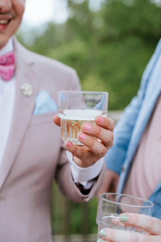 a woman holding a glass of champagne with a man in a pink suit behind her