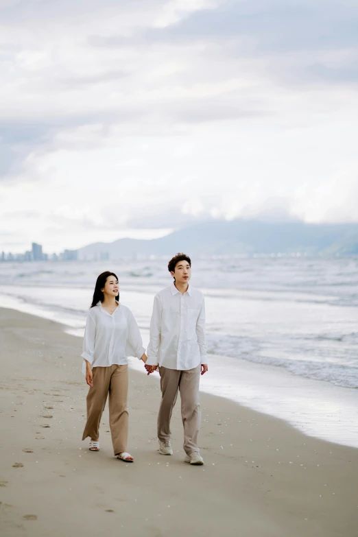 man and woman holding hands walking along an ocean beach