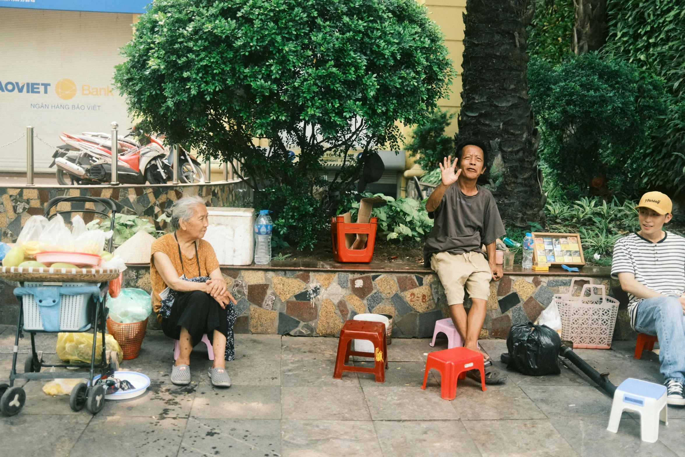 three men sitting on a sidewalk holding their hands up to the sky