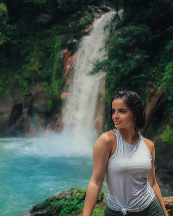 a woman with long hair is standing near a waterfall