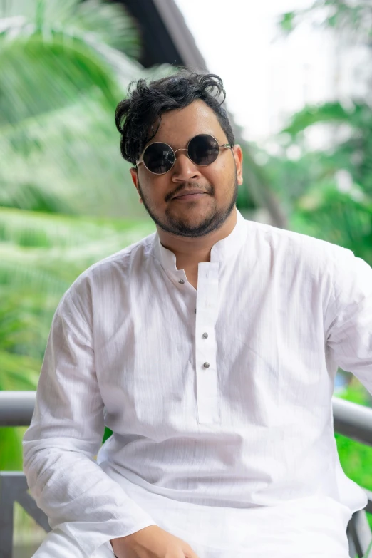 man sitting down wearing sunglasses and a white shirt