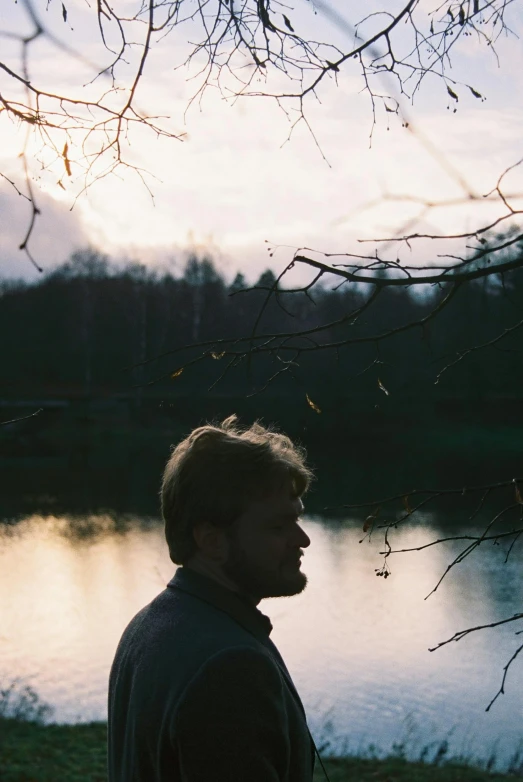 a young man standing on the grass near a body of water