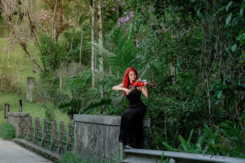 a woman with red hair is playing a violin by the river