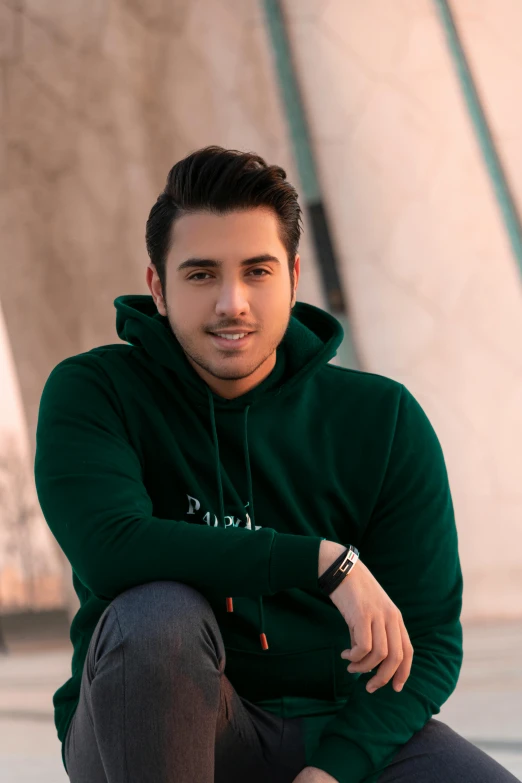 a man posing with his legs crossed and a green sweatshirt on