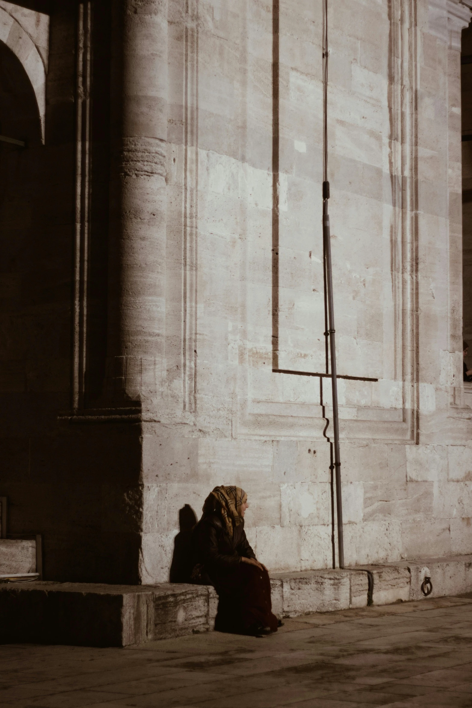 a person sitting on the sidewalk by a tall building