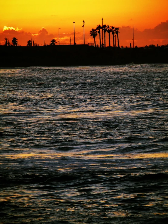 the sun is setting over the water with trees in silhouette