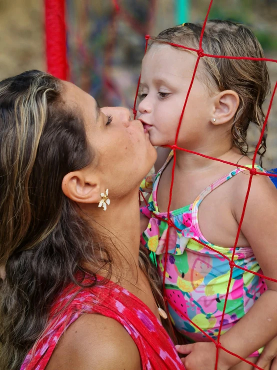 woman kissing little girl with caged background in urban setting