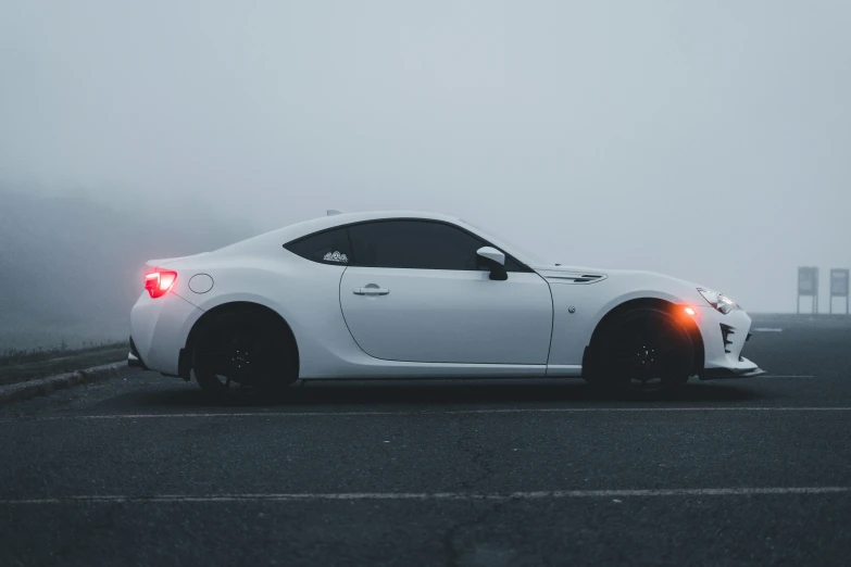 a white sports car is driving on a foggy day