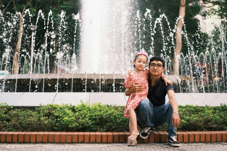 the man and the little girl is taking a po in front of a fountain