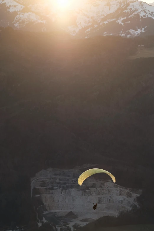 a paraglider glides across the mountains while the sun sets