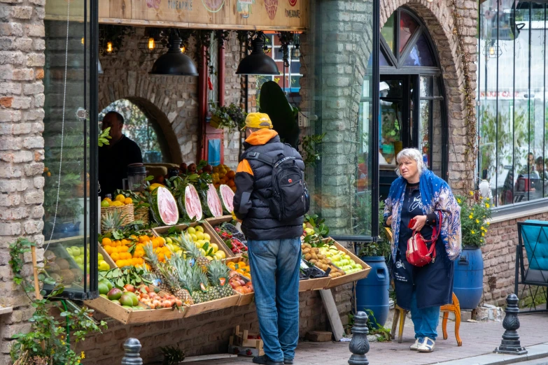 a group of people are outside of a store selling fruits and vegetables