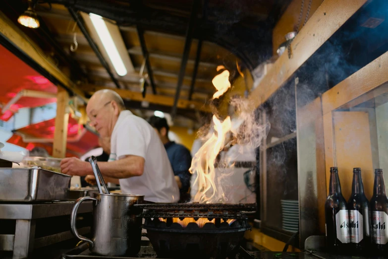 an old man making food on a grill next to bottles