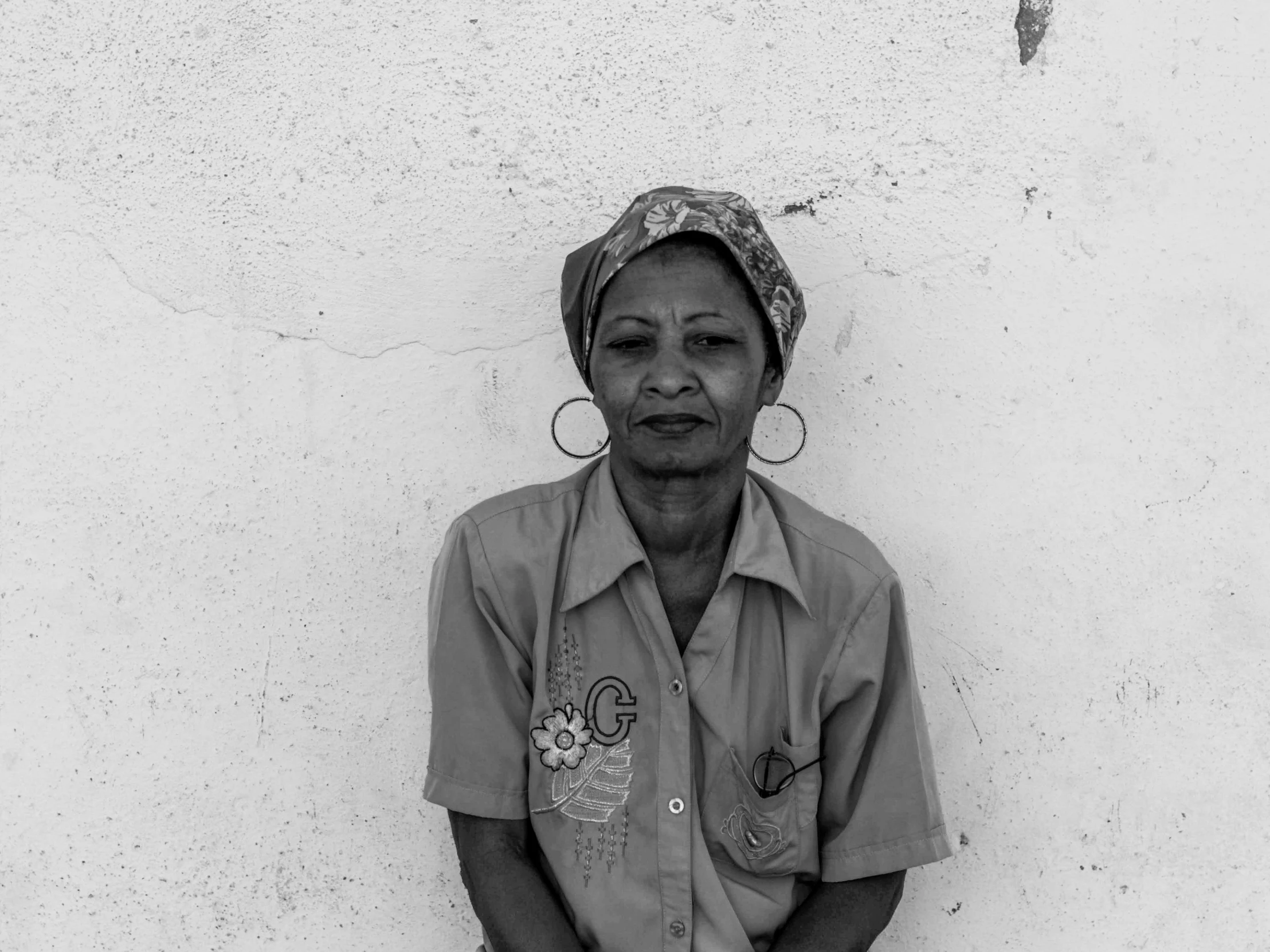 an older black woman is sitting against a white wall