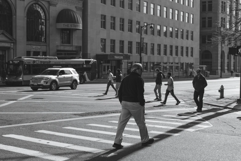 several people walk across a crosswalk as traffic goes by