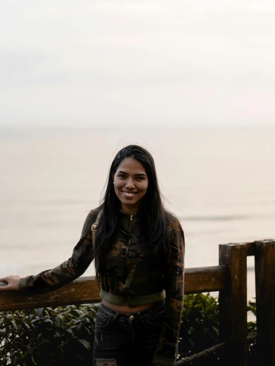 a smiling young woman standing near a wooden fence