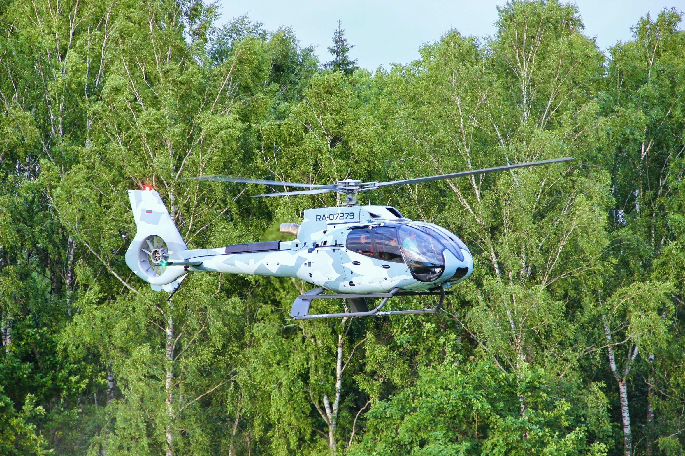 a large helicopter flying over a forest filled with green trees