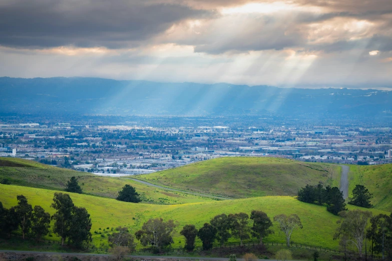 sunlight shines through the clouds over a lush green hillside