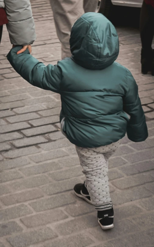 a young child holding the arm of an adult while walking on a brick sidewalk