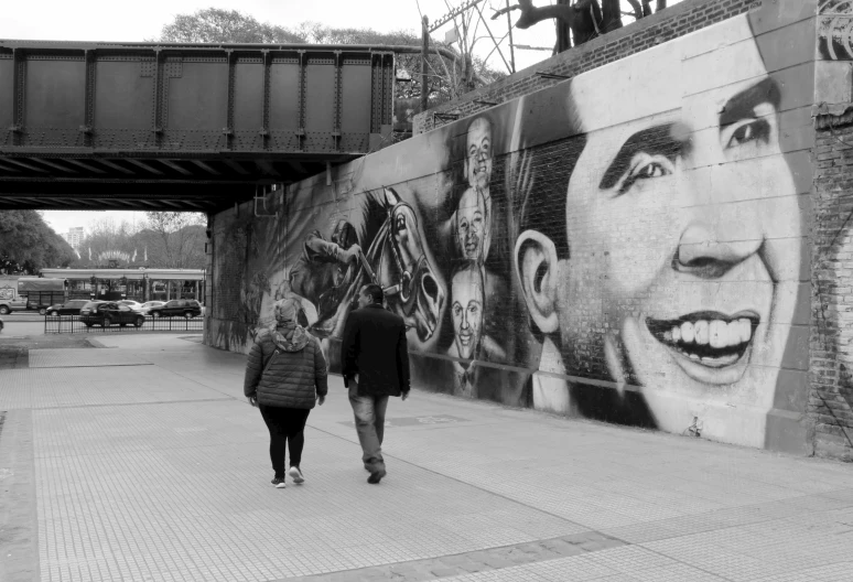 two people walk near a large wall with murals on it