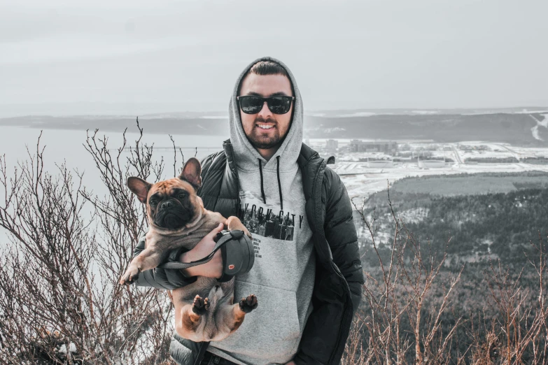 a man holding his dog in his arms on top of a mountain