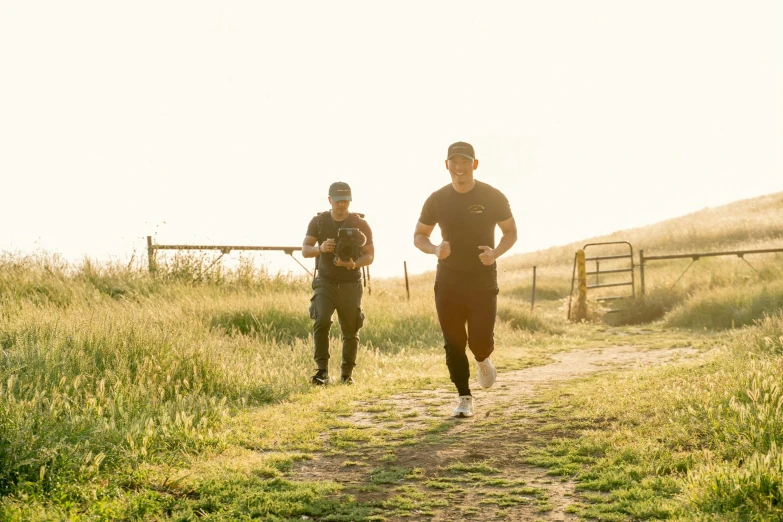 two men on trail running in open area with gate