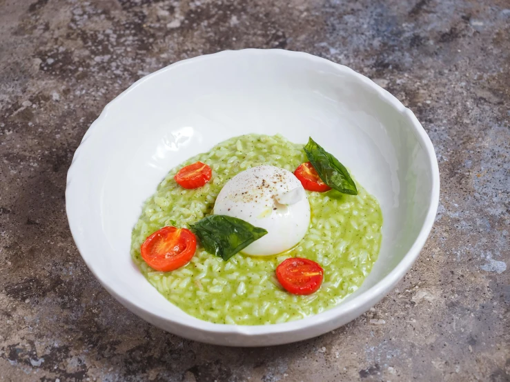 there is a bowl of green soup with eggs and tomatoes on top