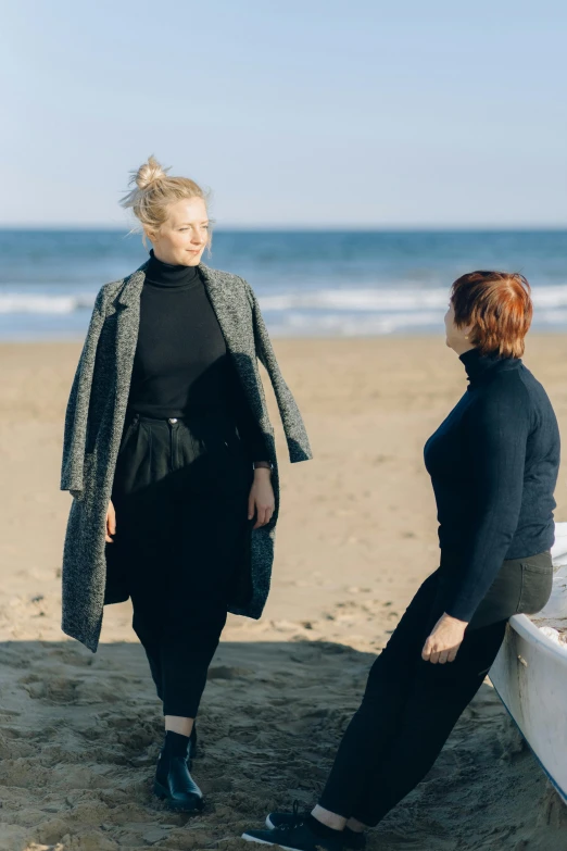 two woman walk on the beach while one of them is looking at the water