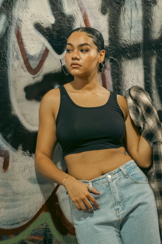 the woman wearing jeans is leaning against a graffiti wall