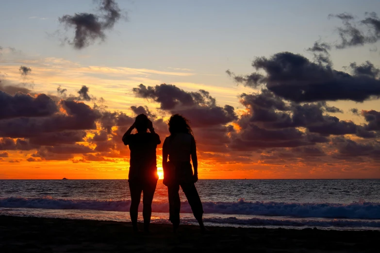 two people standing in the water looking at the sunset