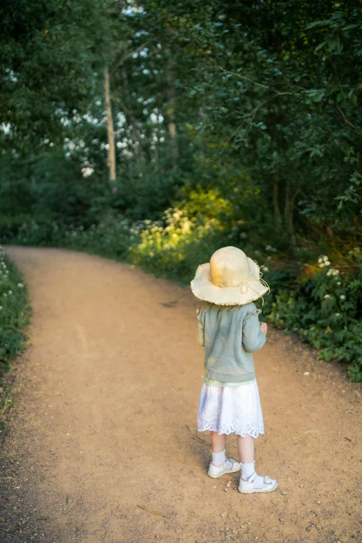 a child stands at the edge of a dirt path as she looks at green plants