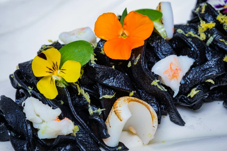 a plate with flowers and shells with black pasta on it