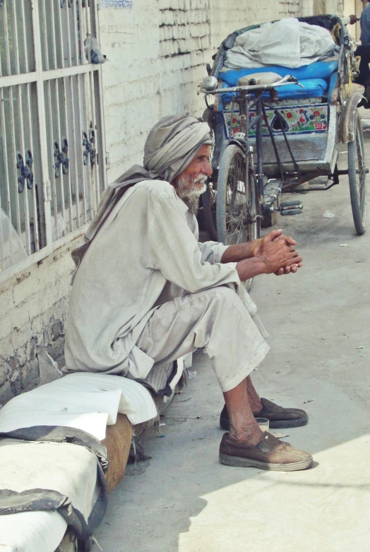 an old man with long hair and grey beard sitting on a wall