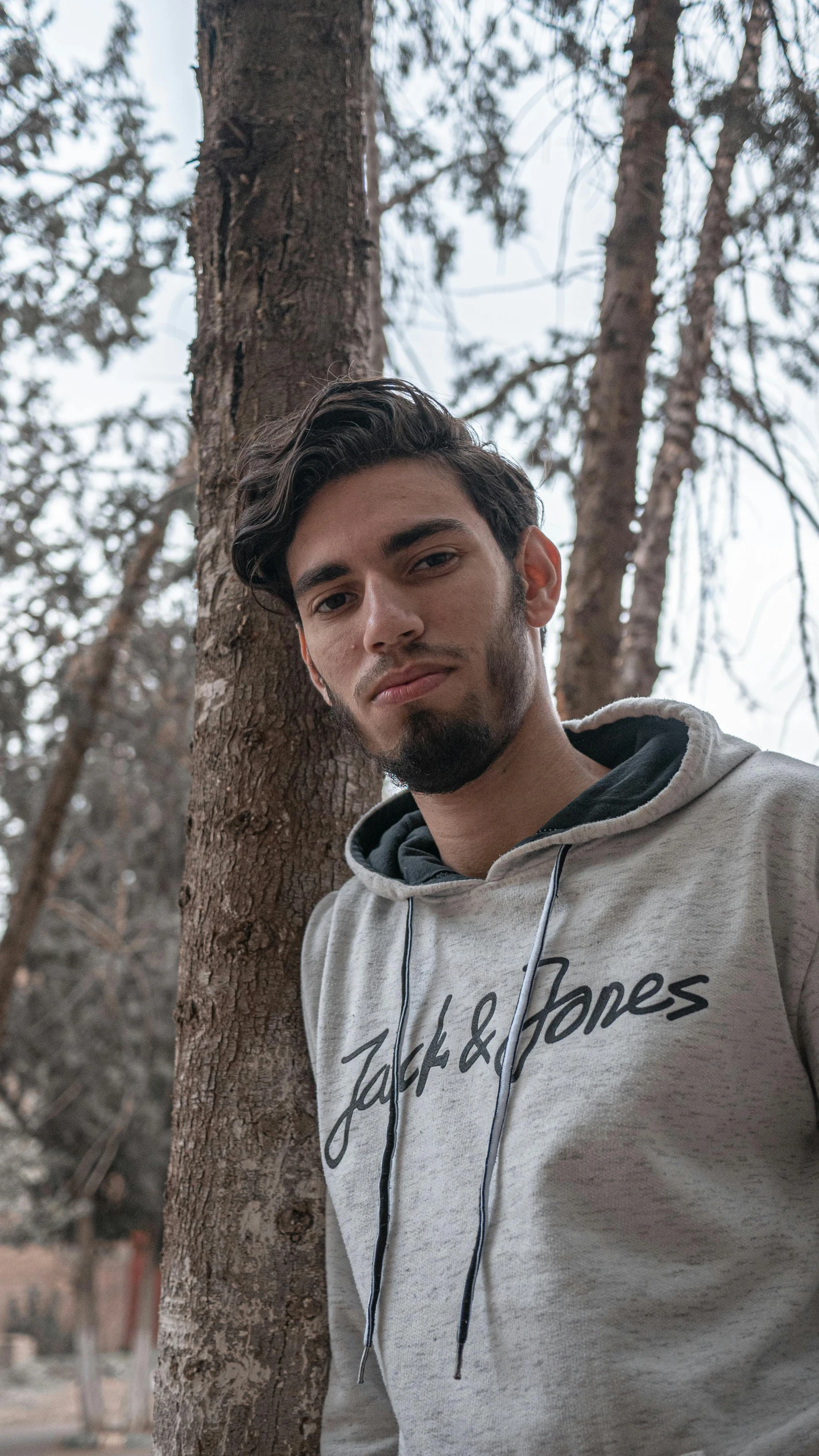 a man standing next to a tree wearing a grey shirt