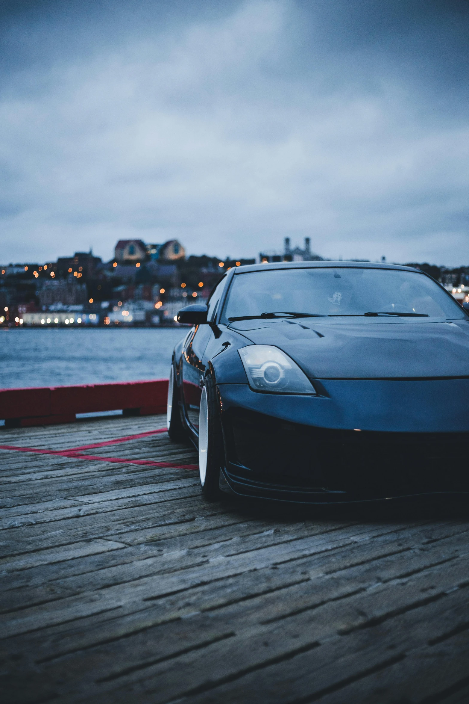 a blue sport car parked on a pier next to water