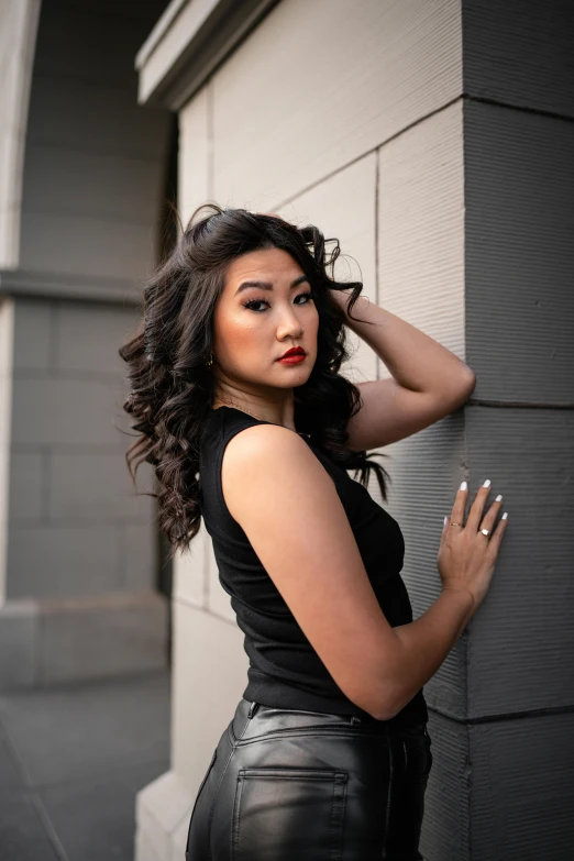 a woman posing against a wall wearing leather