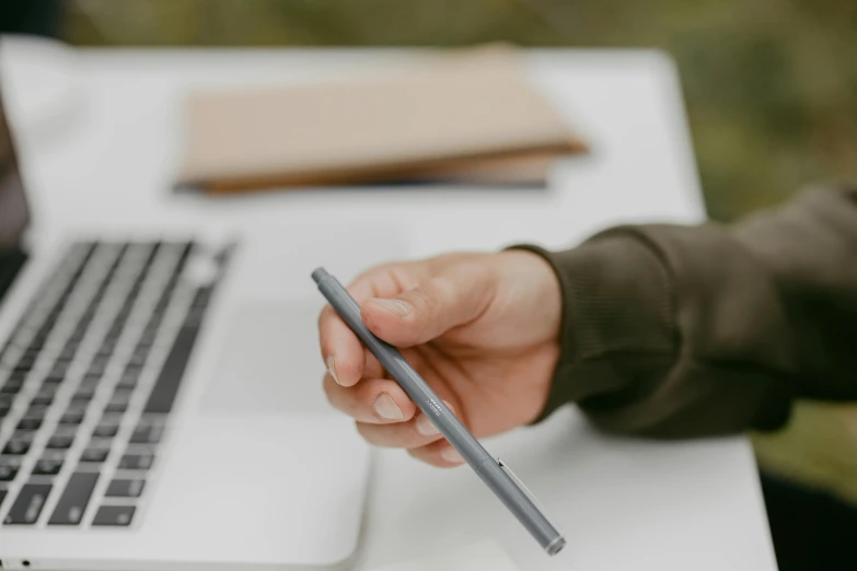 a hand holding a pen and pointing at it on top of a laptop computer