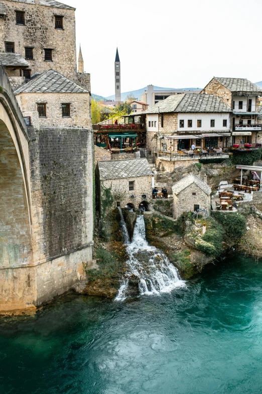 the old bridge has an arched stone wall and water cascading down it