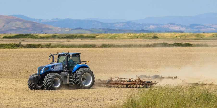 blue and black tractor in an open plain with dirt and plants